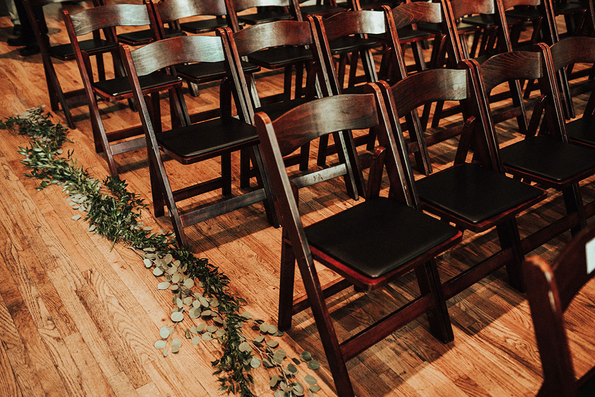 Dark Wooden Ceremony Seating with Greenery Aisle