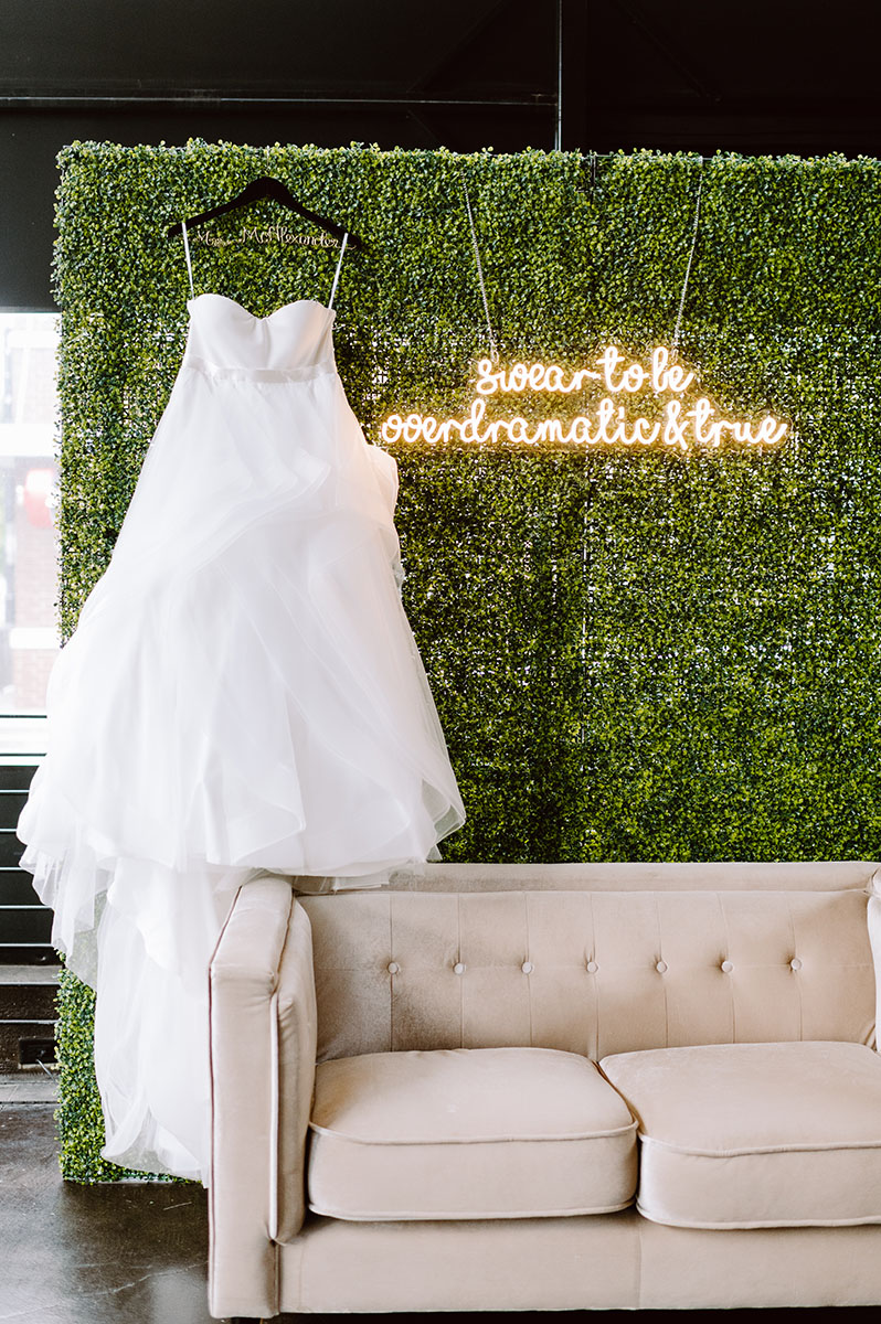 Sarah's Dress hanging against her greenery wall Photo Booth with neon sign of Taylor Swift song lyrics