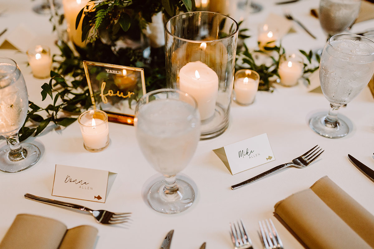 A table setting with acrylic table numbers, candle centerpieces, and greenery decor