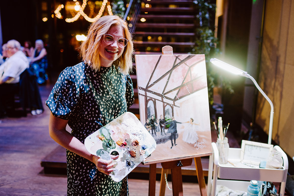 A live painter poses next to the finished painting of Sarah and Patrick's first dance at their wedding reception
