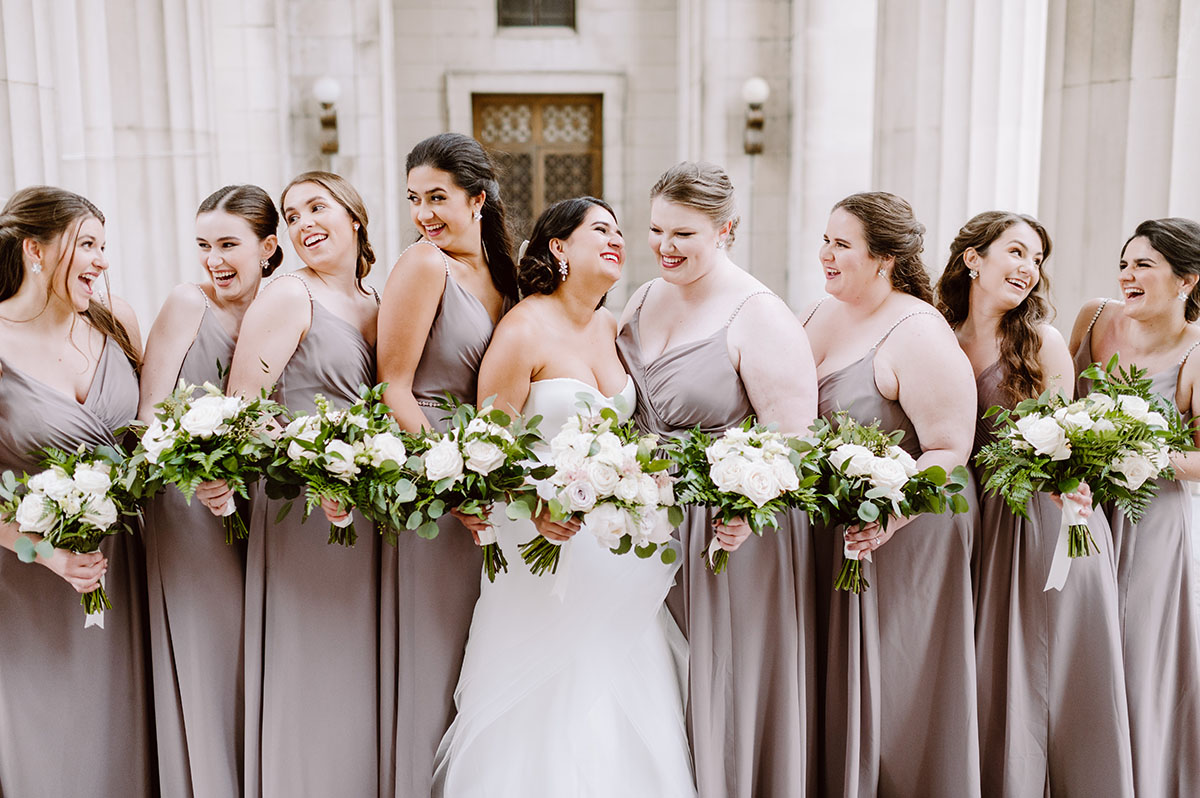 Sarah and her Bridesmaids in matching taupe dresses. Each is holding a bouquet of white blooms and greenery.
