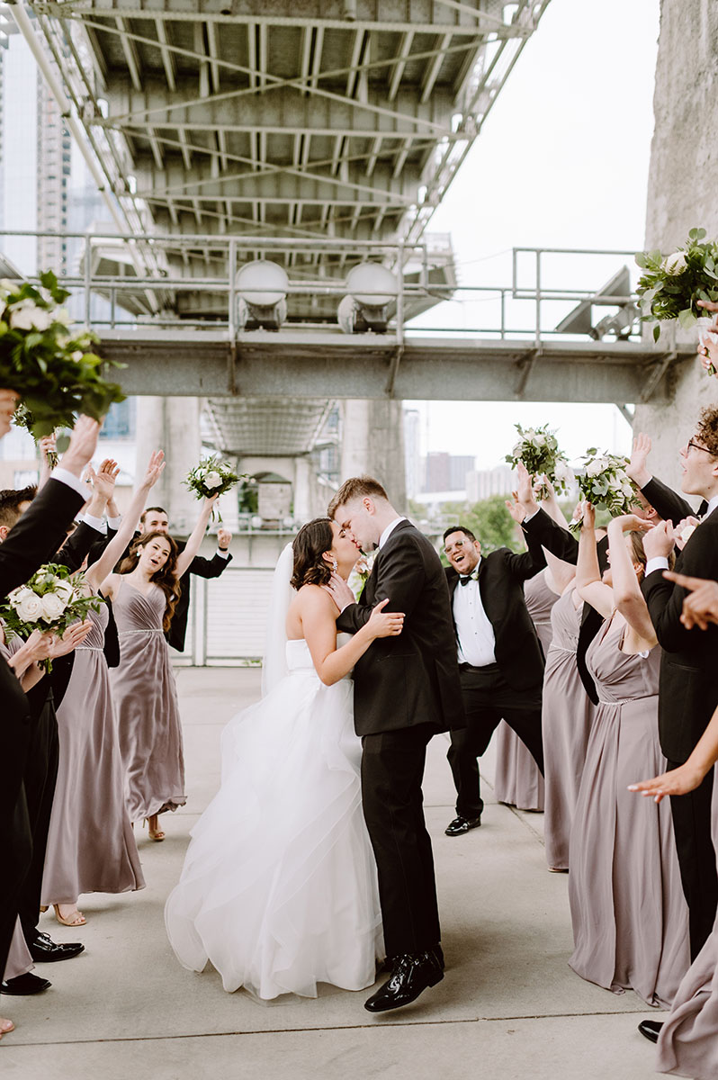 Sarah and Patrick kissing underneath the Nashville pedestrian bridge while their wedding party cheers