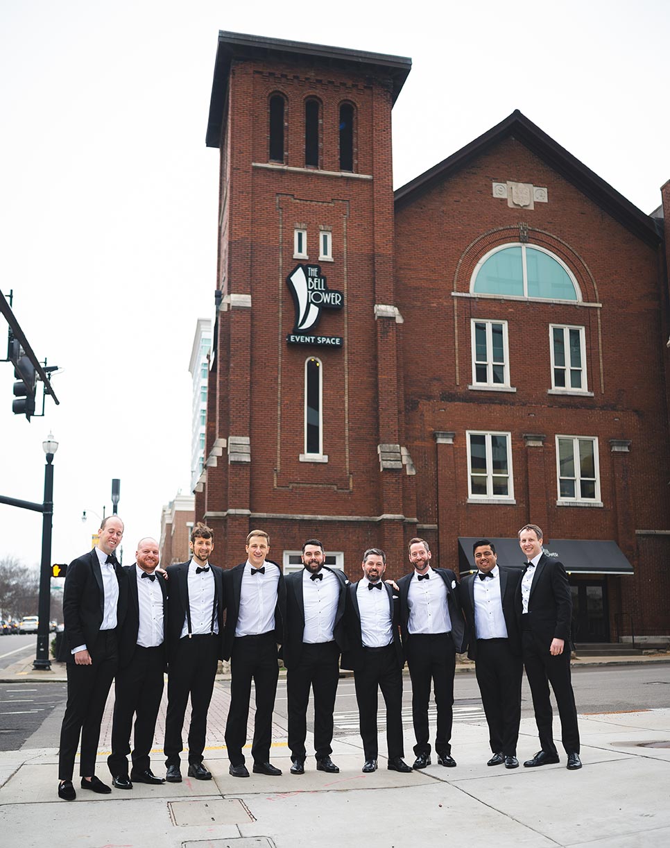 Groomsmen pose for photos in tuxedos outside the The Bell Tower