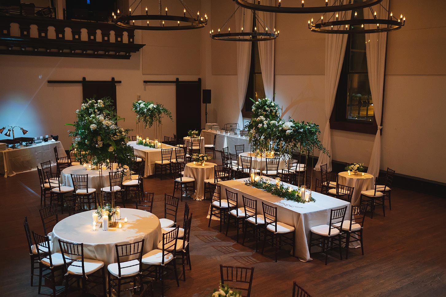 Reception with white linens elevated floral centerpieces and hanging goblet chandeliers