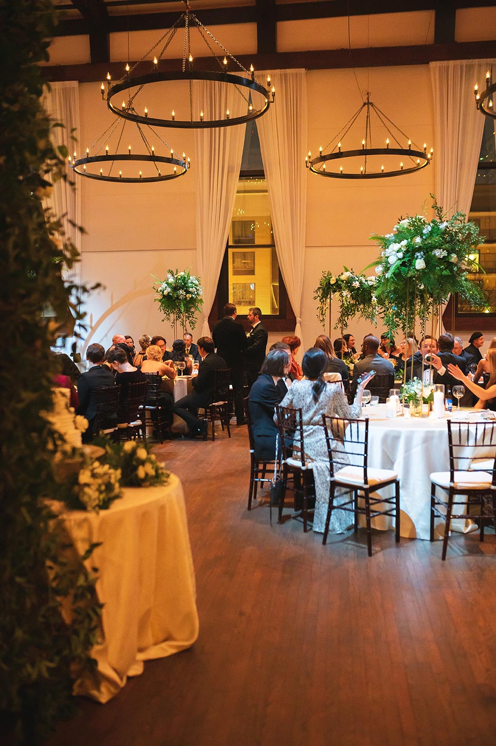 Reception with white linens elevated floral centerpieces and hanging goblet chandeliers