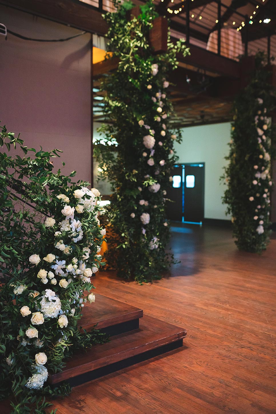 Floral display with greenery and white roses on the stairwell and entrance pillars