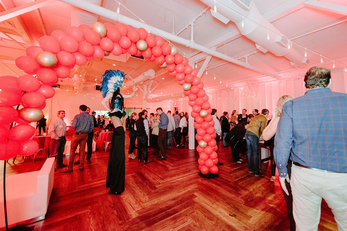 Stilts walker underneath red and gold balloon arch for corporate event