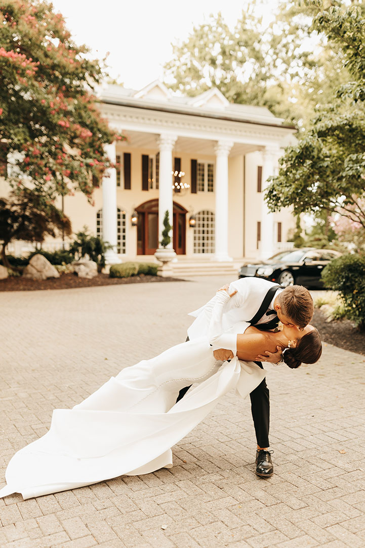 Bride and groom kissing in front of the Estate at Cherokee Dock