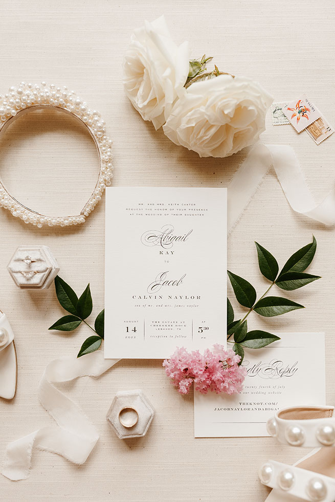 Classic and Elegant Bridal Details with Invitation Suite | Champagne Florals with Greenery, Pearl Earrings and Headband | Wedding and Bridal Accessory Flat Lay