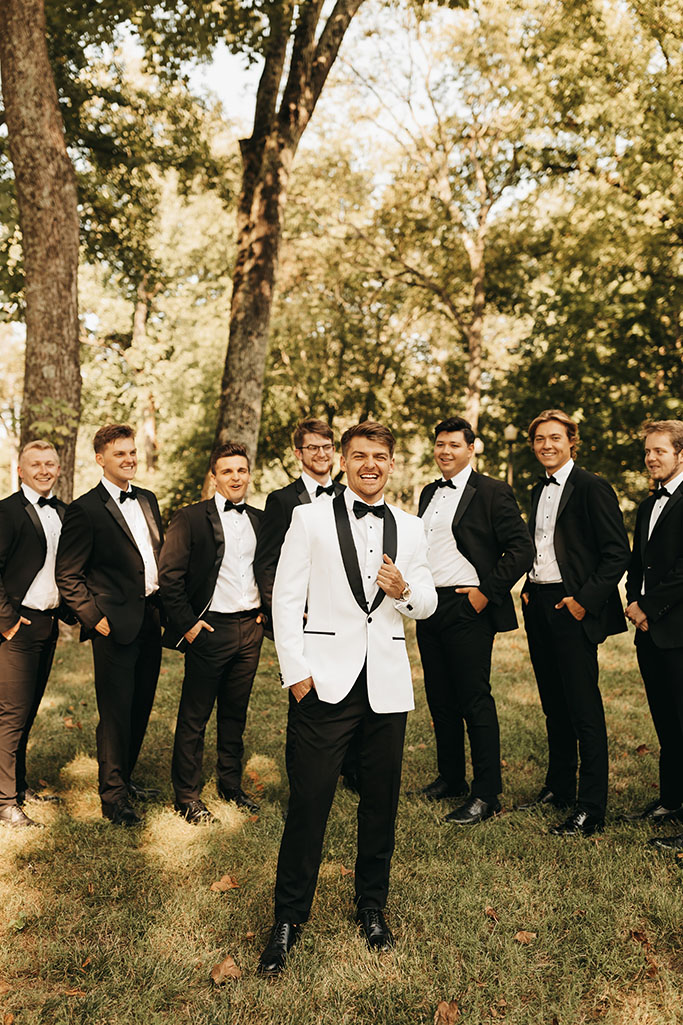 groom in classic white tuxedo and groomsmen in black tuxedos