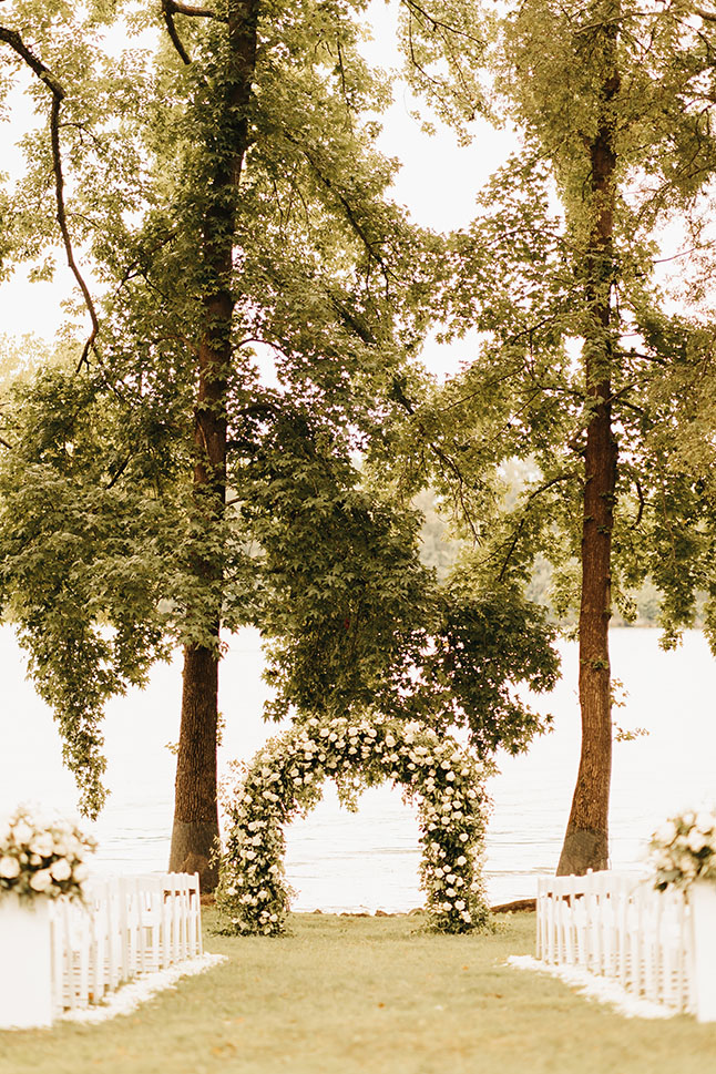 lakeview wedding ceremony with white floral arch with greenery