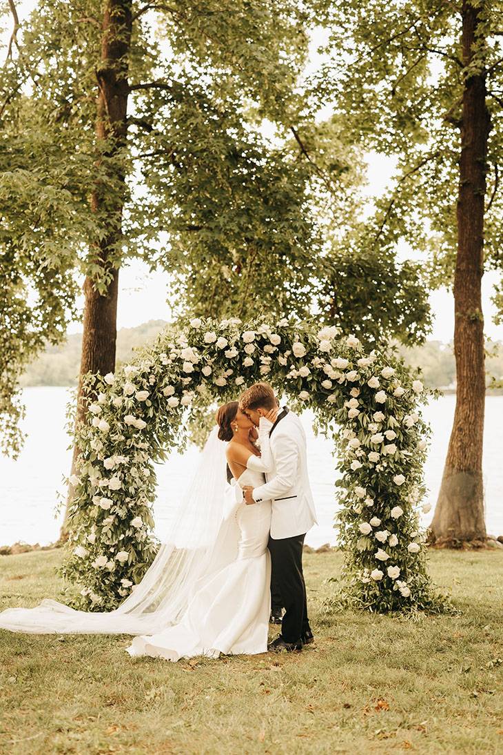 Bride and Groom Kissing Beneath Classic Wedding Floral Arch at Cherokee Dock