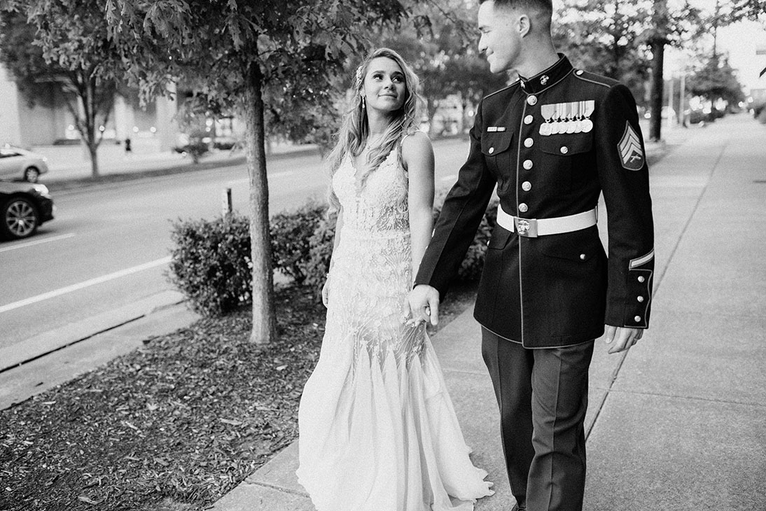 groom in military uniform holds brides hand outside the bell tower in downtown nashville