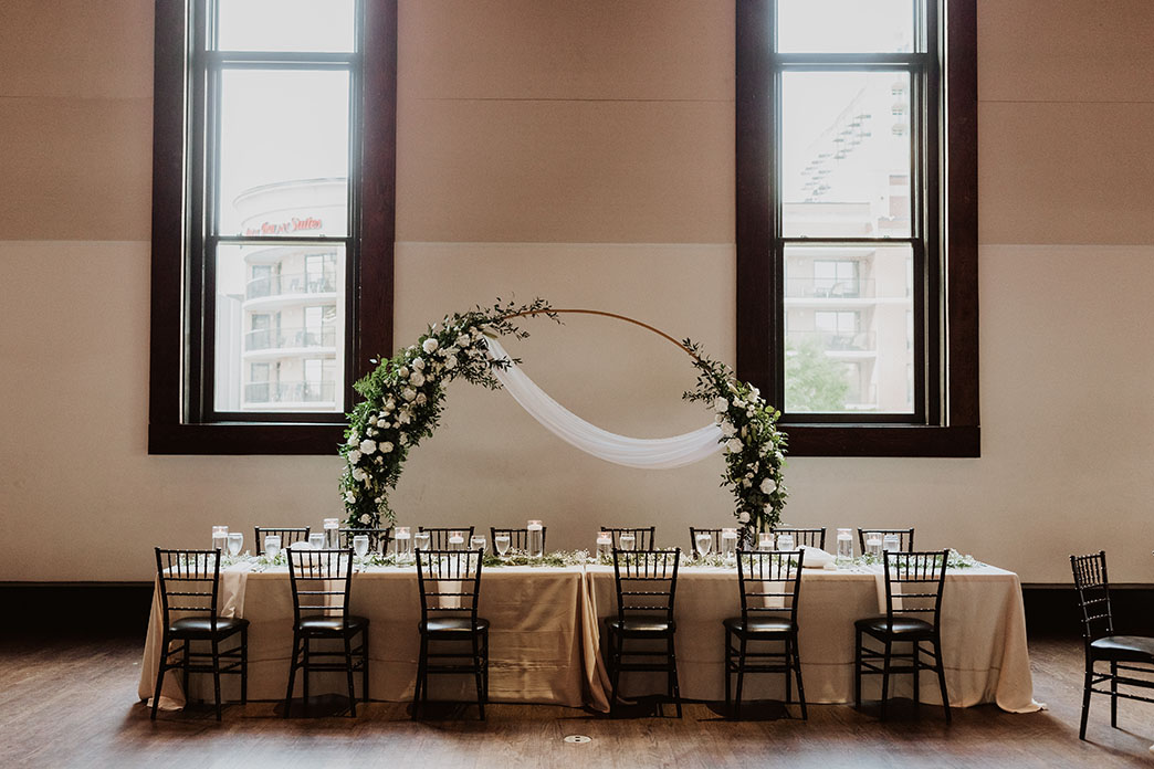 wedding reception head table with floral arch and greenery between the grand windows