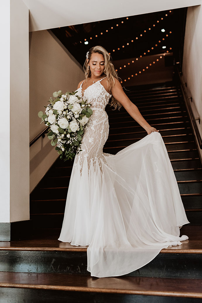 bride poses on staircase with cascading white floral bouquet