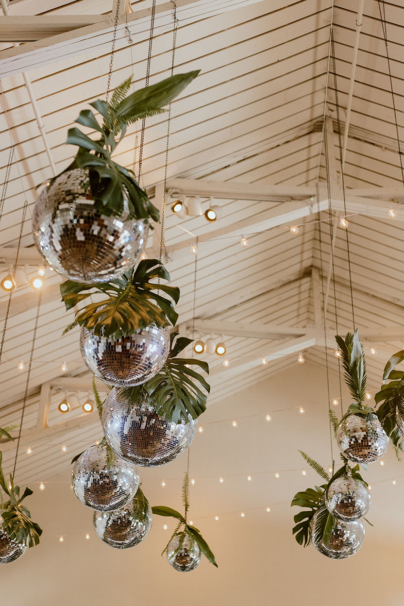 Summer wedding reception disco balls decorated with tropical leaves