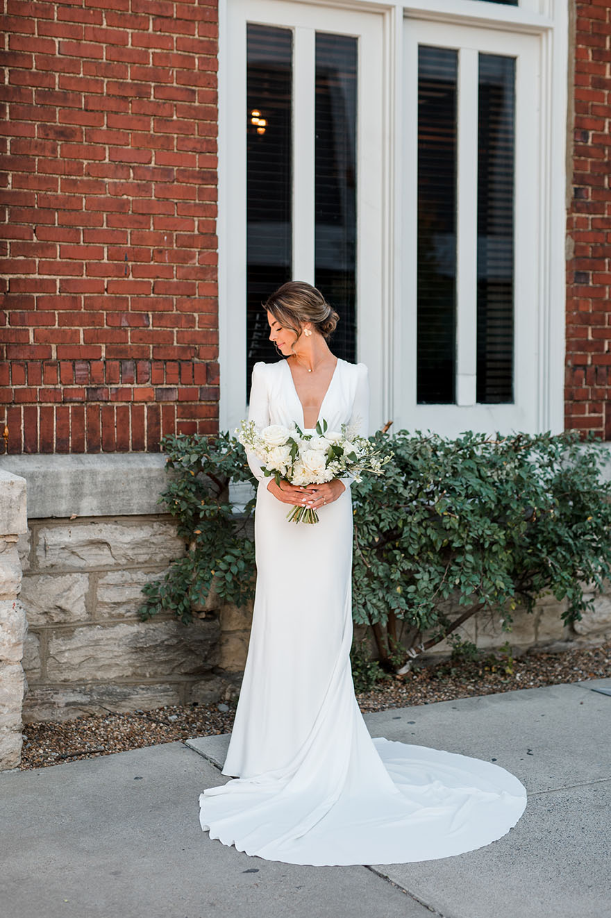 bride in modern low cut gown with long sleeves holding a white floral bouquet