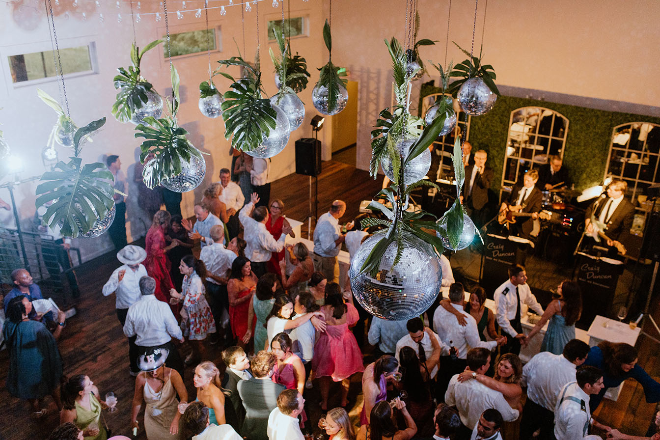 Wedding Guests Dancing at The Cordelle under disco ball installation with Tropical Summer Greenery