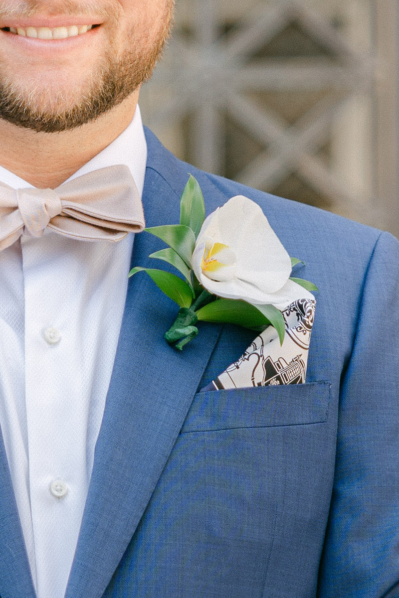 Close-up of groom's white flower boutonniere and patterned pocket square in a blue suit with ivory bow tie
