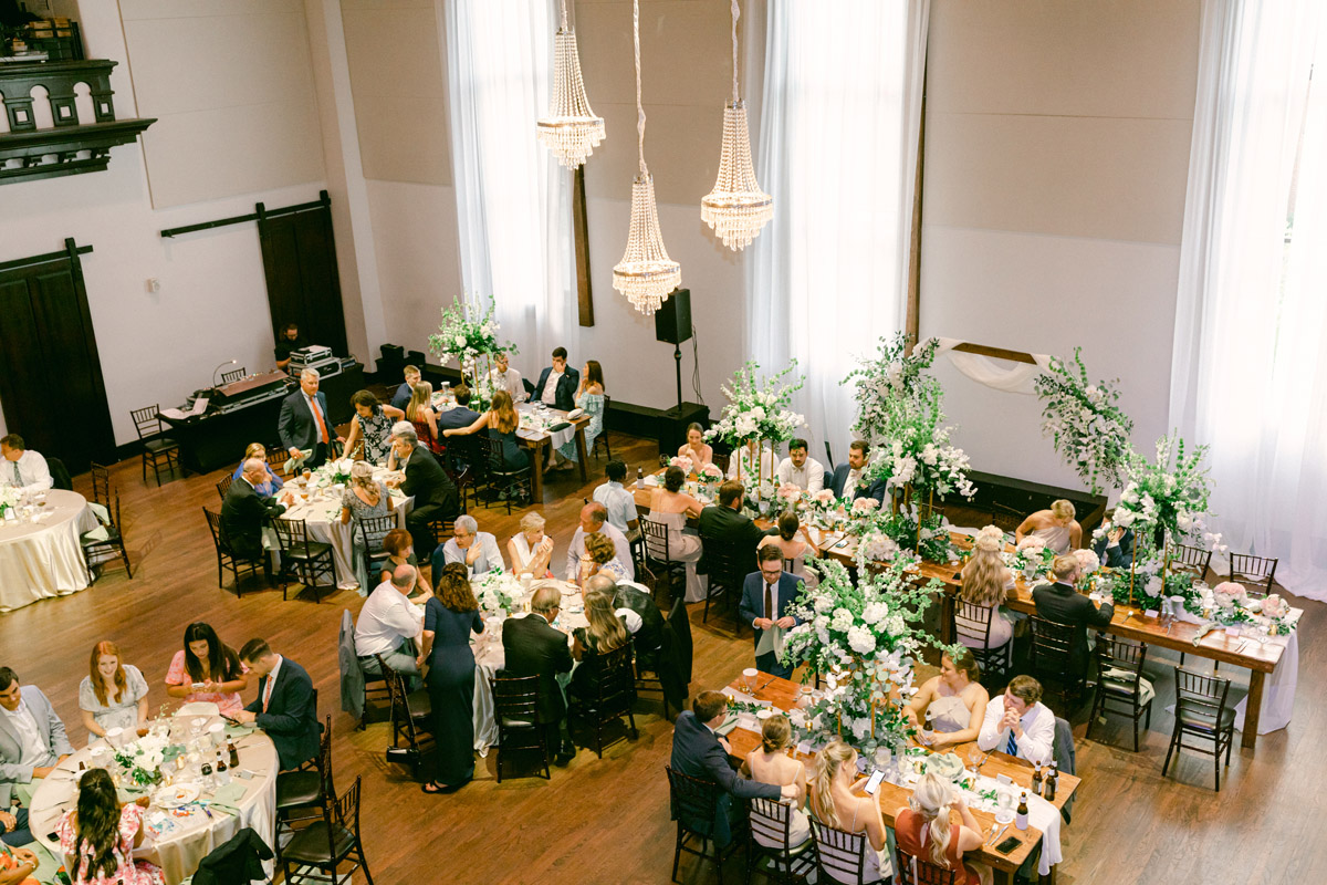 Bird eye view of wedding reception filled with people at dinner tables and 3 chandeliers hanging above