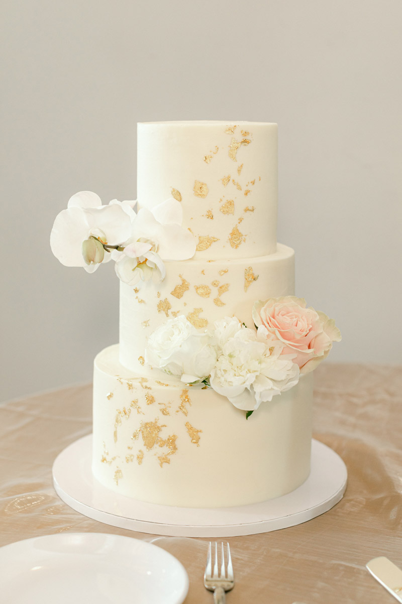 Three-tier classic white wedding wake with white orchids and roses with gold leaf detailing