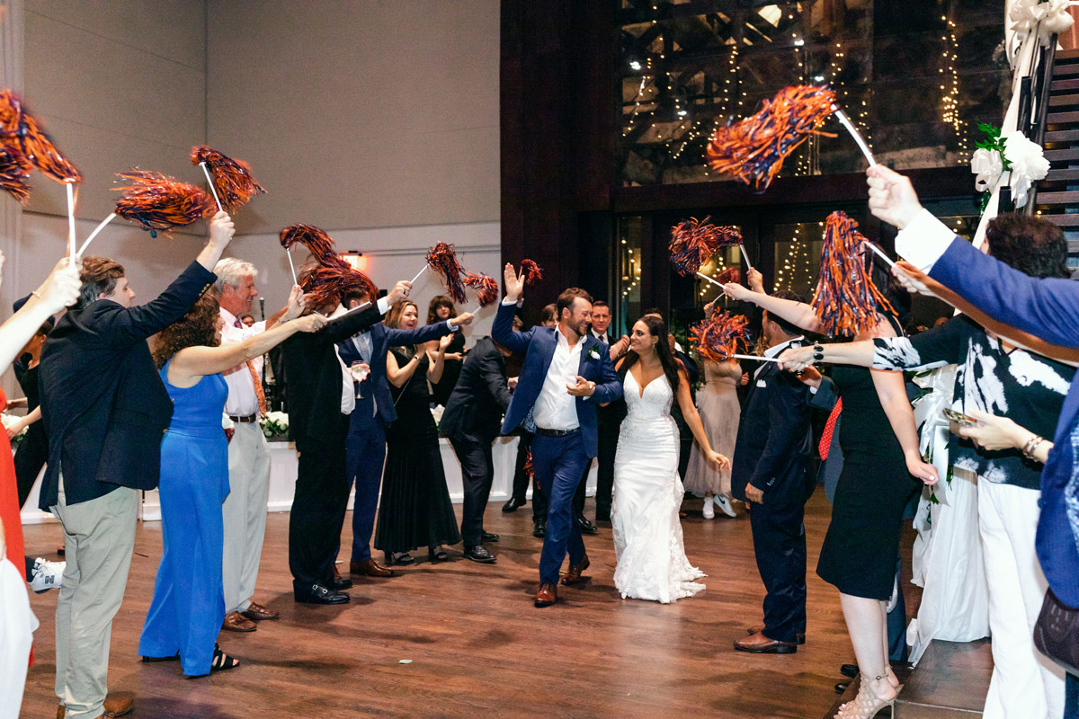 Bride and groom exit wedding reception as guests wave pom poms with Auburn University's colors
