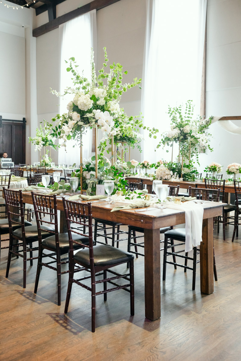 Wedding reception table with elevated floral centerpiece in gold stand with white blooms and whimsical greenery