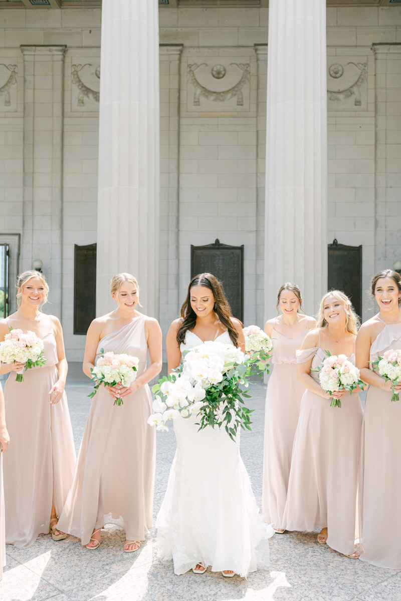 Bride poses with bridesmaids who are wearing soft blush dresses