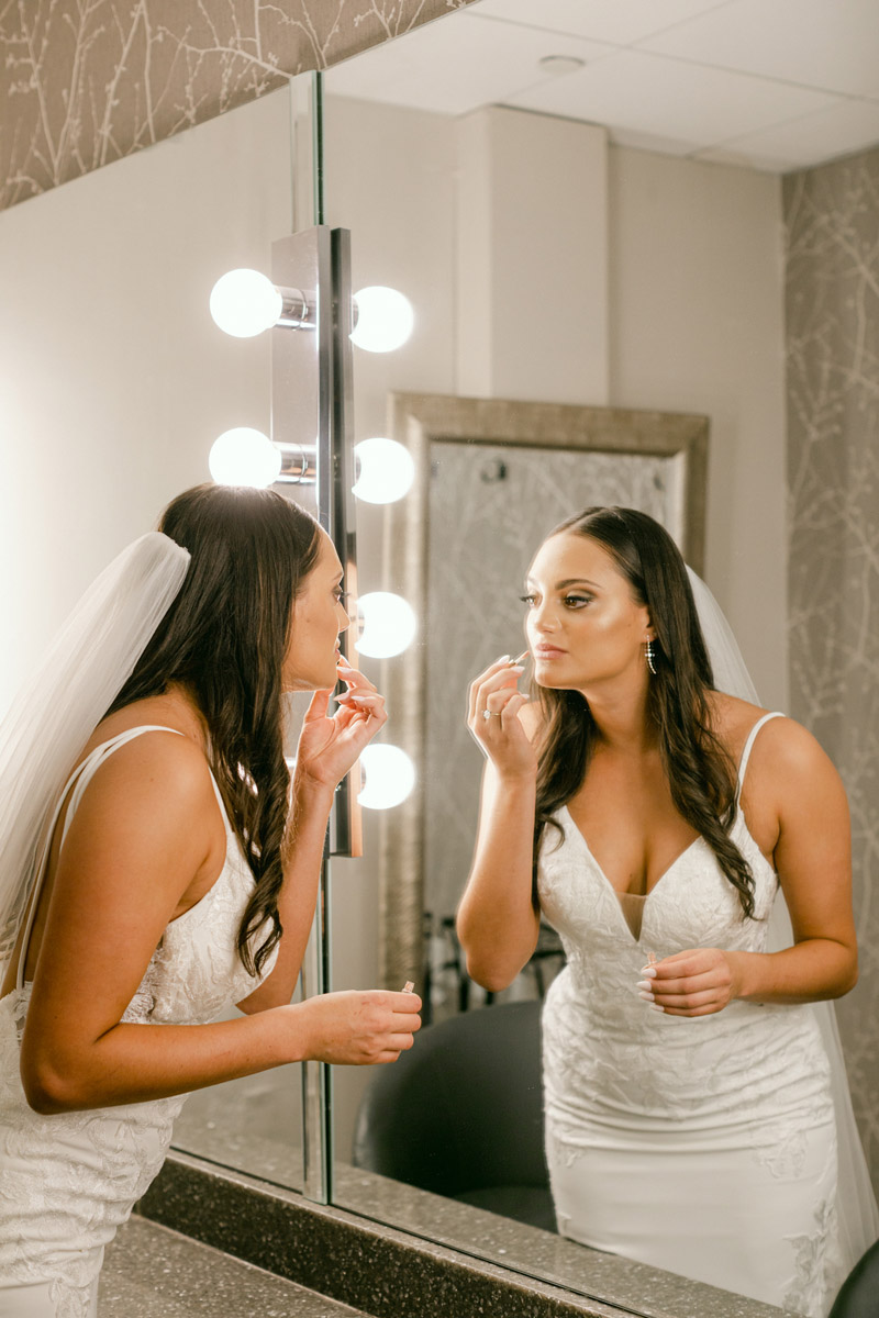 Bride fixing lip gloss in large mirror before the ceremony begins