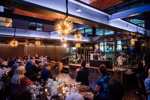Corporate dinner under starburst chandeliers, with a speaker at a podium addressing guests at candlelit tables