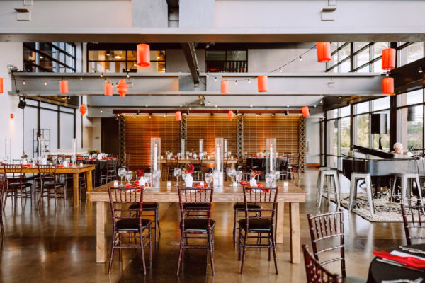 Dinner party at long wooden tables under red paper lanterns in an industrial event space