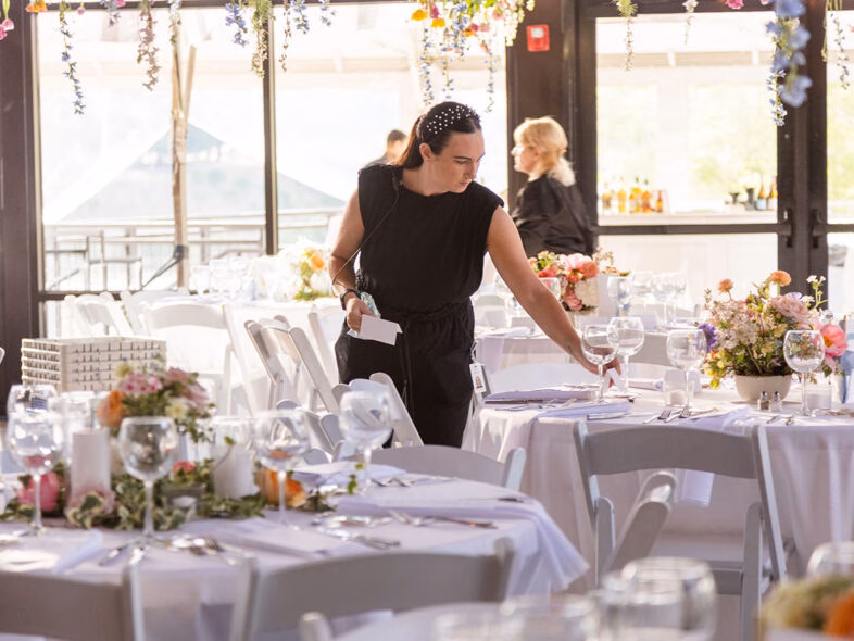 Event planner setting a reception table with white linens, glassware and pastel centerpieces