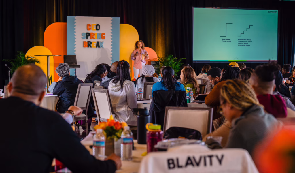 Attendees at a CEO Spring Break conference watching a speaker on stage in front of a large presentation screen