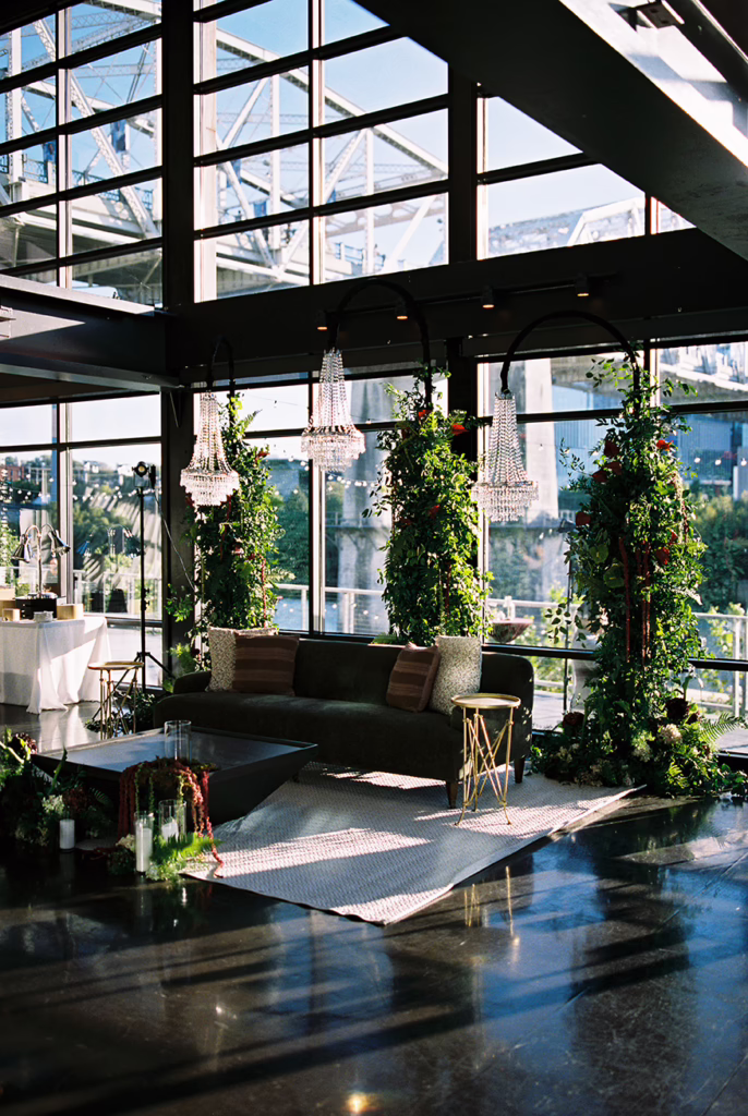 Glass-walled ceremony space with columns of greenery, a hanging crystal chandelier and river views