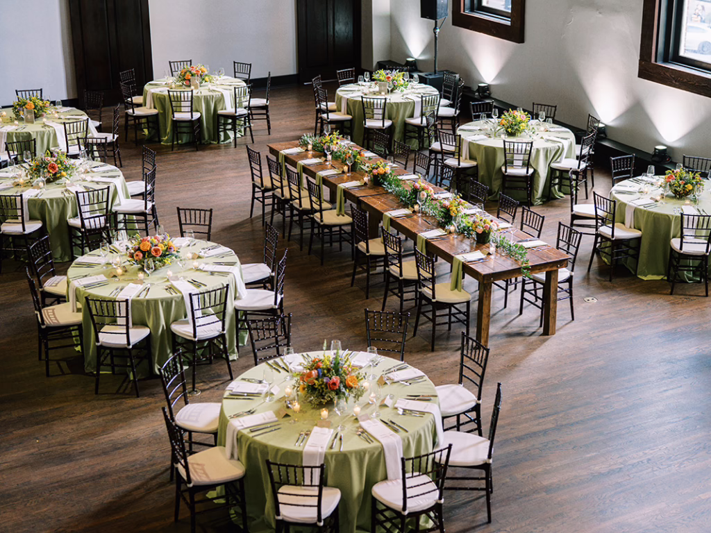 Banquet room with round tables in sage-green linens, black chiavari chairs and floral centerpieces