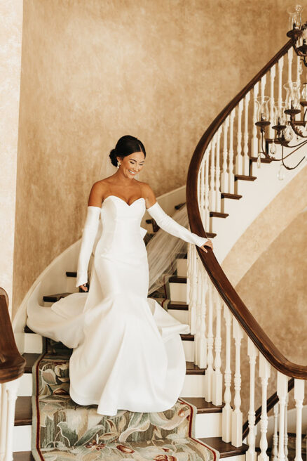 Bride walks down a spiral staircase at Nashville wedding venue Cherokee Dock wearing strapless sweetheart gown and gloves