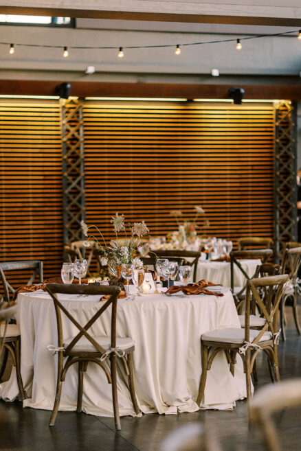 Neutral wedding table setting with crossback chairs and rust-colored napkins