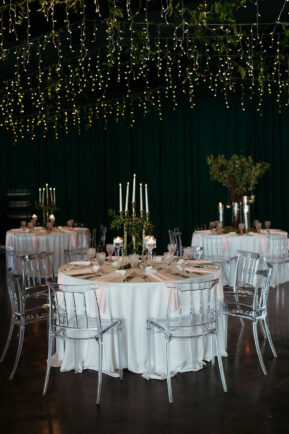 Gold candelabra centerpiece on reception tables with clear ghost chairs and ivory linens