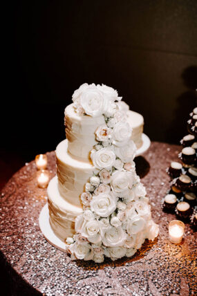 White Wedding Cake covered in flowers sitting on rose gold sequin linen