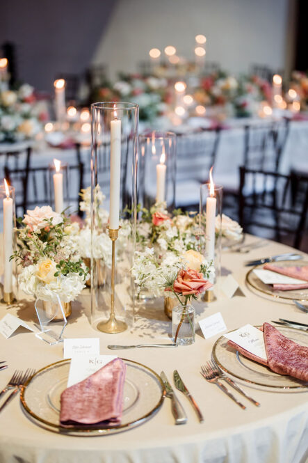 delicate gold details, lush floral arrangements in hues of white and pink with verdant greenery, the soft glow of candles