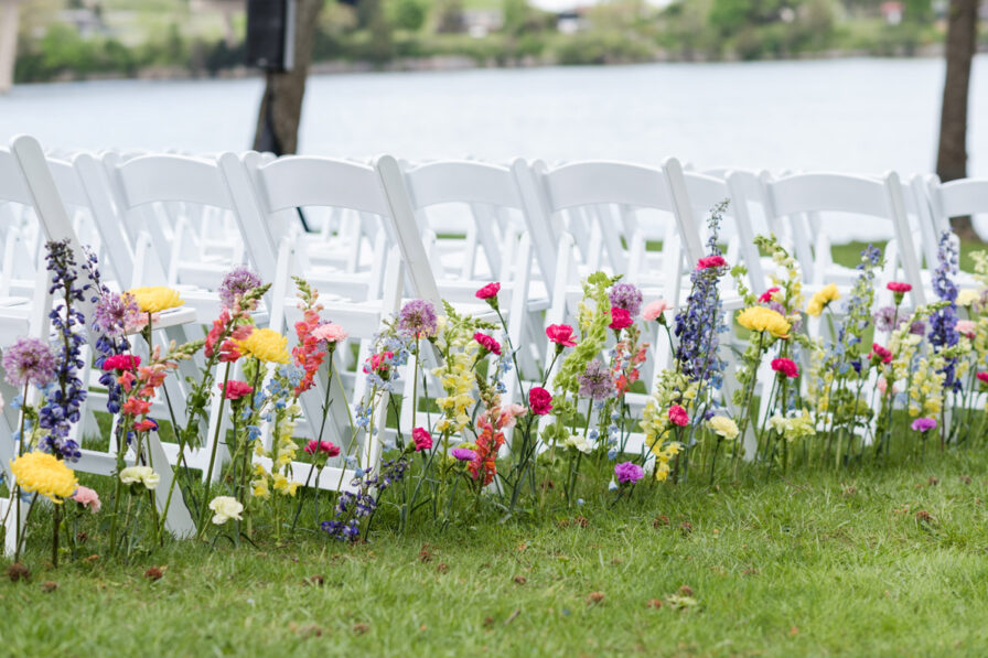 Colorful florals lining outdoor wedding ceremony aisle