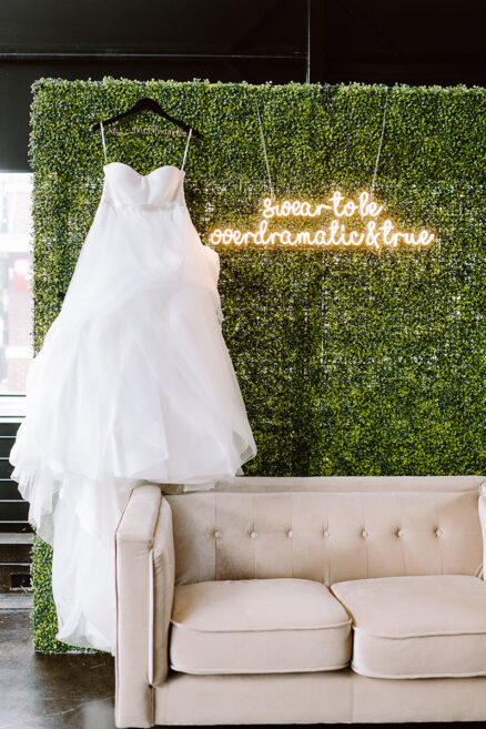 Sarah's Dress hanging against her greenery wall Photo Booth with neon sign of Taylor Swift song lyrics